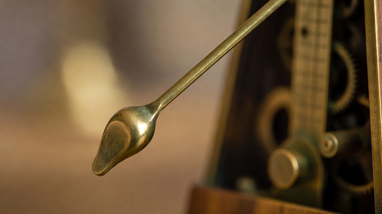 Close-up of a brass metronome pendulum frozen mid-swing with a soft blurred background